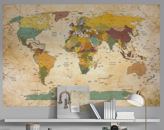 Pode incluir: Um adesivo de parede com um mapa do mundo de estilo vintage com um visual desgastado e envelhecido. O mapa está em cores suaves e apresenta as fronteiras e os nomes dos países. O mapa é exibido em uma parede cinza acima de uma mesa branca com uma lâmpada, livros e outros elementos decorativos.