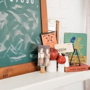 May include: A vintage chalkboard with white lettering and numbers, framed in wood. The chalkboard is propped up on a white shelf, alongside books, apples, and vintage ephemera, creating a nostalgic schoolhouse theme.