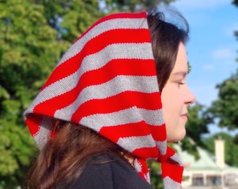 May include: A woman wearing a red and gray striped knit hooded scarf. The scarf is tied at the neck and the hood is pulled up over her head.