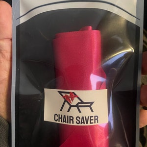 May include: A roll of bright red satin ribbon, packaged in a clear plastic bag. The label reads "CHAIR SAVER" with a graphic of a chair and bow. The ribbon is tightly rolled and ready for use.