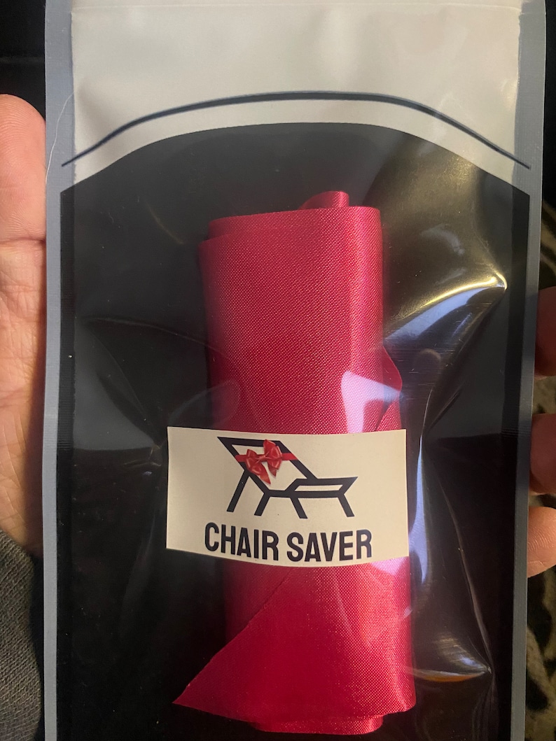 May include: A roll of bright red satin ribbon, packaged in a clear plastic bag. The label reads "CHAIR SAVER" with a graphic of a chair and bow. The ribbon is tightly rolled and ready for use.