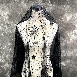 May include: Black sheer fabric with a celestial design featuring stars, moons, and constellations. The fabric is embellished with sequins and beads.
