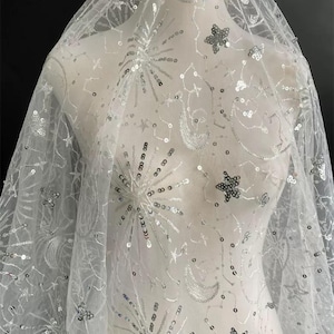 May include: White tulle fabric with silver sequins and embroidery in the shape of stars, moons, and constellations.