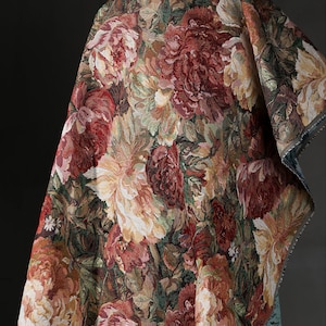 May include: A woven fabric featuring a dense floral pattern with large, detailed blossoms in shades of deep red, burgundy, cream, and muted green. The textile displays a complex tapestry-style weave with visible threads and a textured surface.