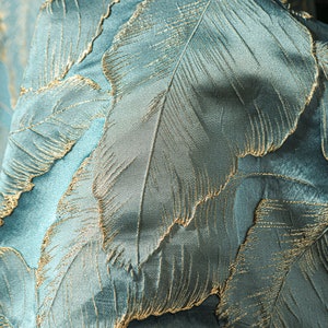 May include: Teal fabric with a gold leaf pattern. The fabric has a subtle sheen and a textured surface.
