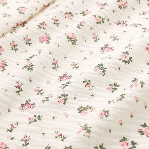 Op de afbeelding: Witte stof met een klein roze bloemenpatroon. De stof heeft een licht getextureerd oppervlak.
