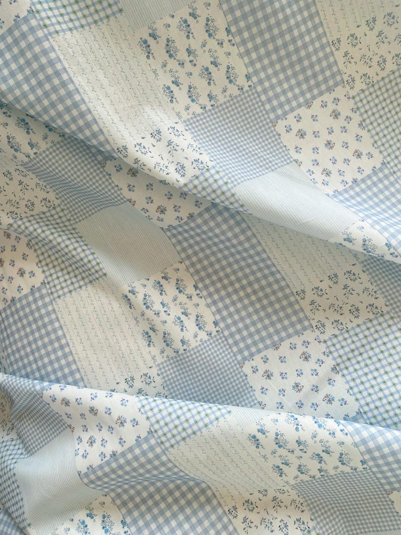 May include: A patchwork quilt featuring a mix of patterns in shades of blue and white. The design includes gingham, floral, and striped sections, creating a textured and visually appealing textile. The quilt is folded, showing the fabric's drape.