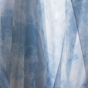 May include: Close-up of a sheer blue and white fabric with a tie-dye pattern. The fabric is draped and folded, creating a soft and airy look.