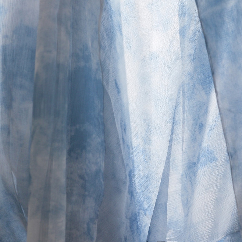 May include: Close-up of a sheer blue and white fabric with a tie-dye pattern. The fabric is draped and folded, creating a soft and airy look.