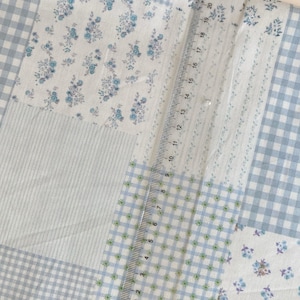 May include: A patchwork fabric with various patterns, including blue gingham, floral prints, and striped sections. A ruler is placed on the fabric, showing measurements up to 23 cm.