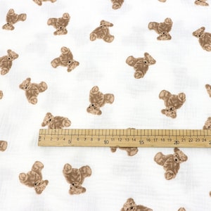 May include: White fabric with a repeating pattern of brown teddy bears. A wooden ruler is placed on the fabric, showing measurements in inches.