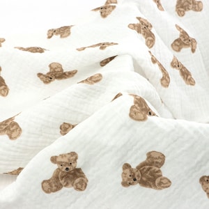 May include: White fabric with a repeating pattern of brown teddy bears. The fabric is soft and textured.