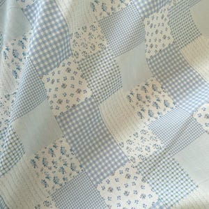 May include: A patchwork quilt featuring a variety of light blue and white fabrics. The quilt incorporates floral, gingham, and striped patterns. The overall design is a mix of textures and patterns, creating a cozy and visually appealing textile.