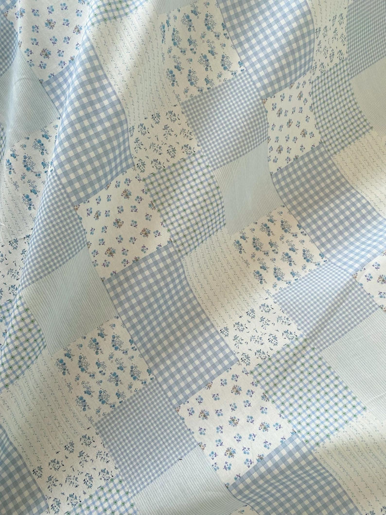 May include: A patchwork quilt featuring a variety of light blue and white fabrics. The quilt incorporates floral, gingham, and striped patterns. The overall design is a mix of textures and patterns, creating a cozy and visually appealing textile.