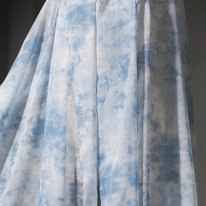 May include: A sheer fabric with a blue and white tie-dye pattern. The fabric is draped and folded, creating a soft and flowing look.