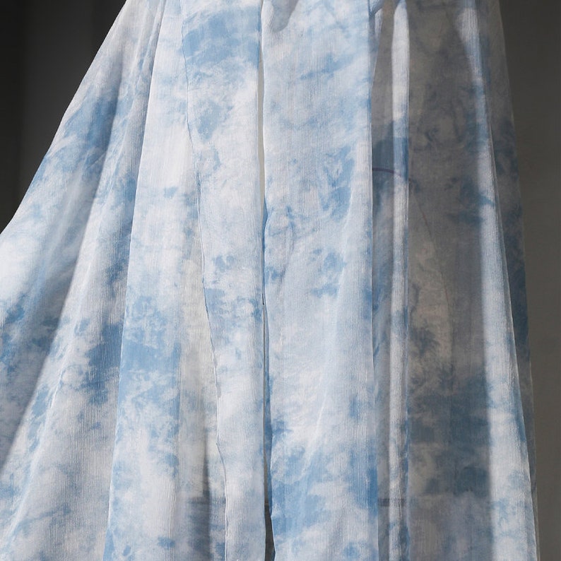May include: A sheer fabric with a blue and white tie-dye pattern. The fabric is draped and folded, creating a soft and flowing look.