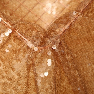 Puede incluir: Primer plano de una tela de lentejuelas doradas con un patrón texturizado y tejido. Las lentejuelas son pequeñas y redondas, creando un efecto brillante.