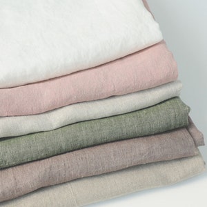 Könnte beinhalten: Ein Stapel aus sechs gefalteten Stoffstücken in verschiedenen Farben, darunter Weiß, Altrosa, Hellgrau, Salbeigrün, Mauve und Beige. Jedes Stoffstück weist eine sichtbare Webstruktur auf und ist ordentlich in einem vertikalen Stapel übereinandergelegt.