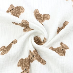 May include: White muslin fabric with a brown teddy bear print. The fabric is soft and lightweight, making it ideal for baby blankets, swaddles, or burp cloths.