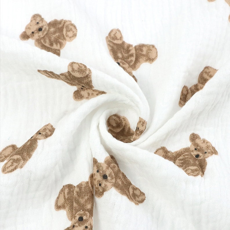 May include: White muslin fabric with a brown teddy bear print. The fabric is soft and lightweight, making it ideal for baby blankets, swaddles, or burp cloths.