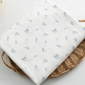 Op de afbeelding: Witte katoenen stof met een klein blauw bloemenprint. De stof is getextureerd en heeft een subtiele glans.