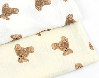 May include: Two folded pieces of fabric featuring a repeating pattern of brown teddy bears. The top layer is white, and the bottom layer is a light cream color. Both pieces of fabric have a soft, textured, and slightly crinkled appearance.