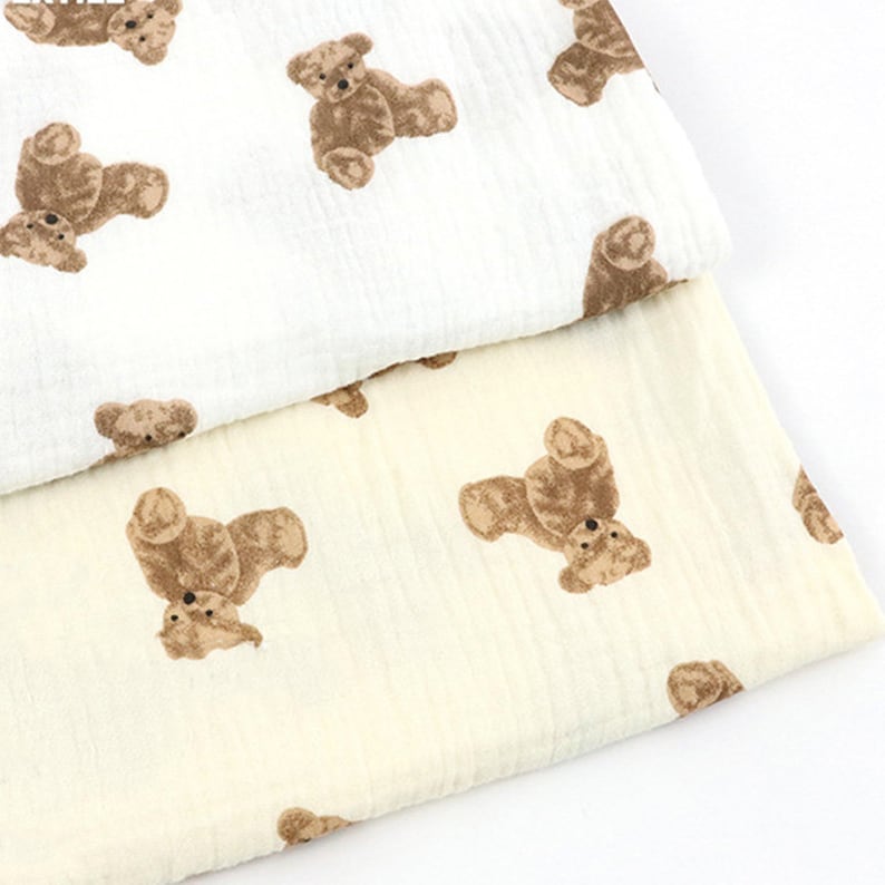 May include: Two pieces of fabric with a brown teddy bear print. The top fabric is white and the bottom fabric is a light cream color.