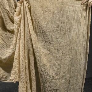 Pu&ograve; includere: Un grande pezzo di tessuto beige con una distinta consistenza verticale stropicciata. Il materiale &egrave; leggero e semi-trasparente, caratterizzato da un bordo grezzo e non rifinito sul lato. Il tessuto cade in pieghe morbide e naturali.
