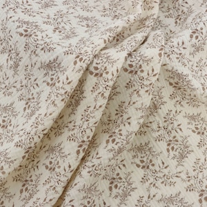 May include: A white fabric with a brown floral pattern. The fabric is soft and has a crinkled texture.