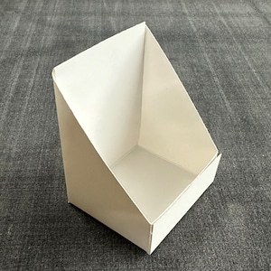 May include: A white cardboard display stand with a triangular front and a rectangular base.