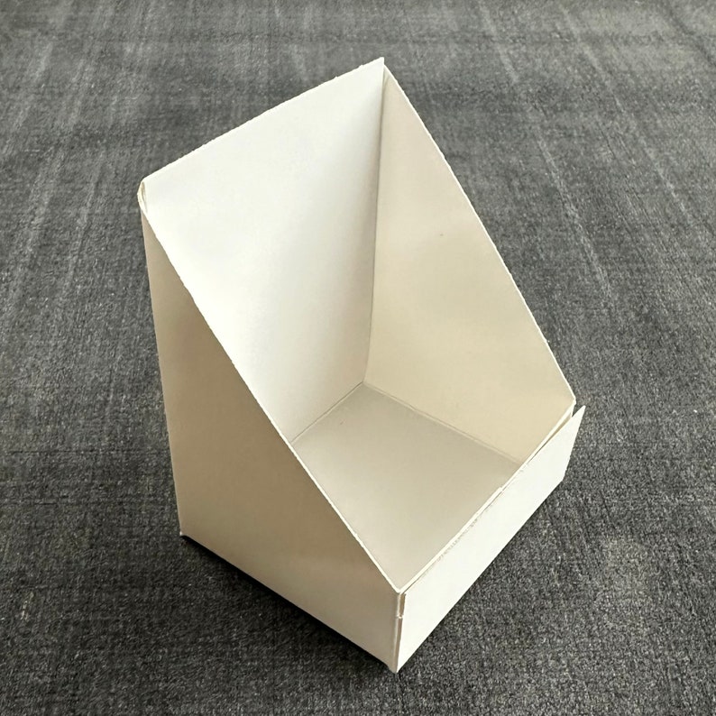 May include: A white cardboard display stand with a triangular front and a rectangular base.