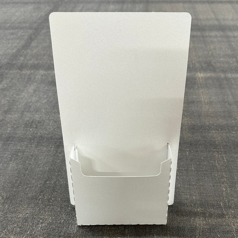 May include: White cardboard countertop display stand with a slot for brochures or flyers.