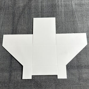 May include: A white paper box template with six panels, ready to be folded and assembled. The template is flat and unfolded, showing all the panels.