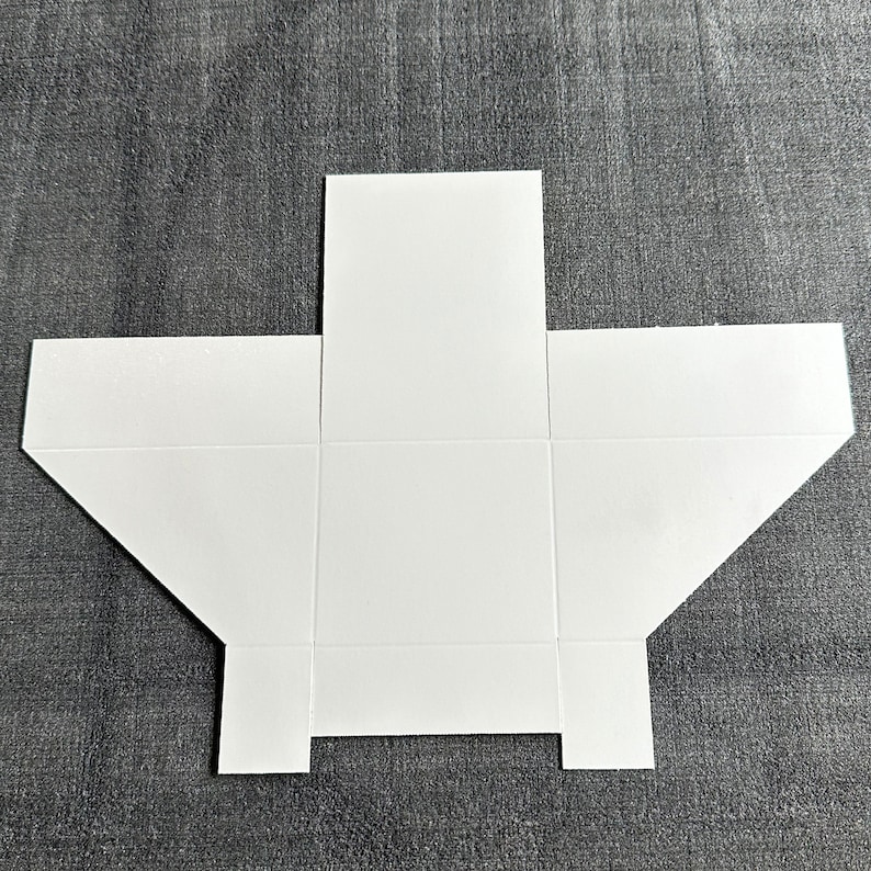 May include: A white paper box template with six panels, ready to be folded and assembled. The template is flat and unfolded, showing all the panels.