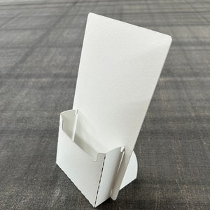 May include: White cardboard countertop display stand with a slot for brochures or flyers.