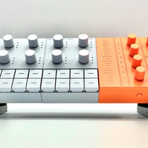 Könnte beinhalten: Ein weißer und orangefarbener elektronischer Musiksynthesizer mit Knöpfen und Tasten. Der Synthesizer hat ein Raster mit Tasten und einen Lautsprecher.