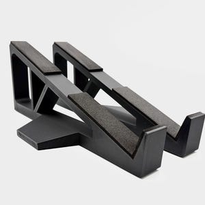 May include: A black laptop stand with a minimalist design. The stand has two angled platforms with textured pads for the laptop to rest on. The base is a solid, geometric shape.