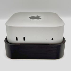May include: A silver Mac mini computer with an Apple logo on top, sitting on a black stand.