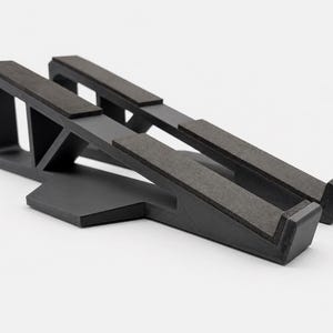 Könnte beinhalten: Ein schwarzer Laptopständer mit angewinkeltem, offenem Rahmendesign und zwei parallelen Stützarmen. Jeder Arm ist mit einer dunkelgrauen, texturierten, rutschfesten Auflagefläche versehen, um ein Gerät zu sichern, ergänzt durch eine breite Basis.