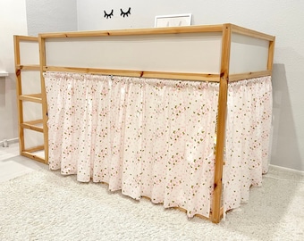 May include: A loft bed frame constructed from light-toned natural wood, featuring a built-in ladder on the left side. The lower section is enclosed by a gathered fabric curtain in white, decorated with a repeating pattern of small pink flowers.
