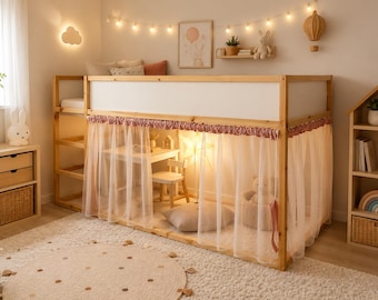 May include: A wooden loft bed with a white upper panel and a sheer, gathered fabric curtain draped around the lower section. The bed frame features a built-in ladder on the left side, creating an enclosed play space underneath with a small table and chair.