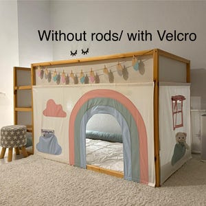 Puede incluir: Un marco de cama de madera con una tienda de tela blanca con un arco iris, nubes y una pancarta colgante. El texto "Without rods/ with Velcro" est&aacute; encima de la cama. Un peque&ntilde;o taburete con un patr&oacute;n de estrellas est&aacute; cerca.