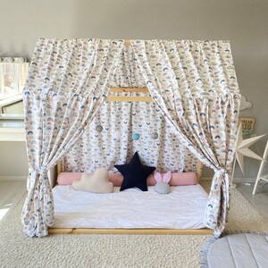 May include: A white canopy bed with rainbow patterned curtains and a white mattress. The bed has a white, pink, and blue pillow on it. The bed is in a room with a white rug and a gray rug with a white border.