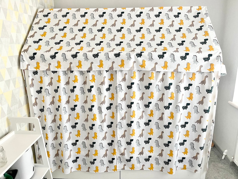 May include: A white fabric canopy with a dinosaur print in black, gray, and yellow. The canopy is made of a soft, lightweight fabric and is perfect for creating a cozy and fun play space for children.