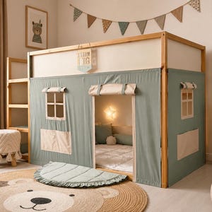 Puede incluir: Una estructura de cama alta de madera con una cubierta de tela verde salvia tipo casita, ventanas enrollables, una entrada central y un letrero colgante que dice TEAM BIG. La estructura incluye una escalera integrada y un techo de tela.