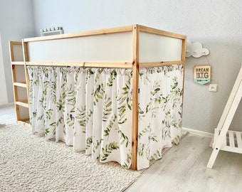 May include: A wooden loft bed frame featuring a white fabric curtain skirt with a green botanical leaf print. The bed includes an integrated ladder on the left side and a solid white panel along the upper section of the frame, creating a play space.