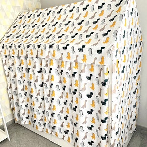 May include: A white fabric canopy with a dinosaur print in black, yellow, and gray. The canopy is draped over a bed frame and has a ruffled edge.