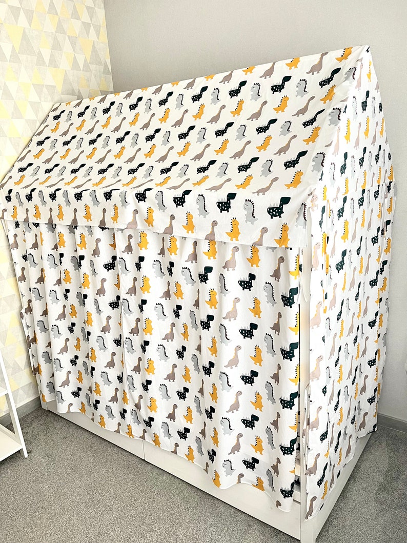 May include: A white fabric canopy with a dinosaur print in black, yellow, and gray. The canopy is draped over a bed frame and has a ruffled edge.
