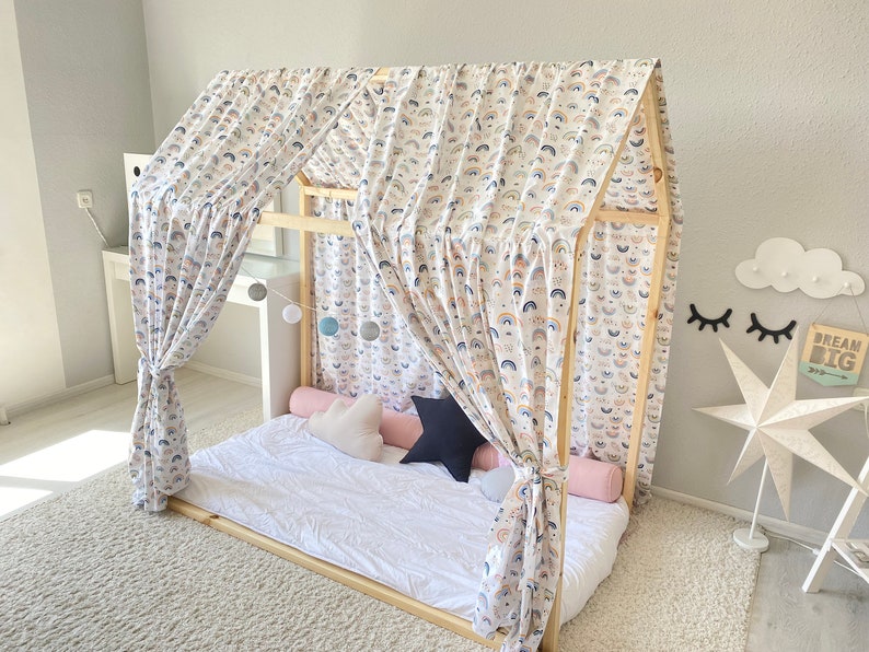 May include: A wooden bed frame with a white canopy featuring a rainbow pattern. The canopy is draped over the bed, creating a cozy and whimsical atmosphere. The bed is made with white bedding and has a few pillows.