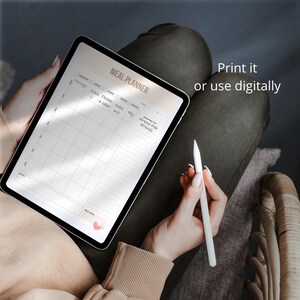 May include: A digital meal planner on a tablet with a white stylus. The planner has columns for breakfast, snack, lunch, snack, dinner, and a shopping list. The text "MEAL PLANNER" is at the top of the planner. The text "Print it or use digitally" is in the upper right corner of the image.
